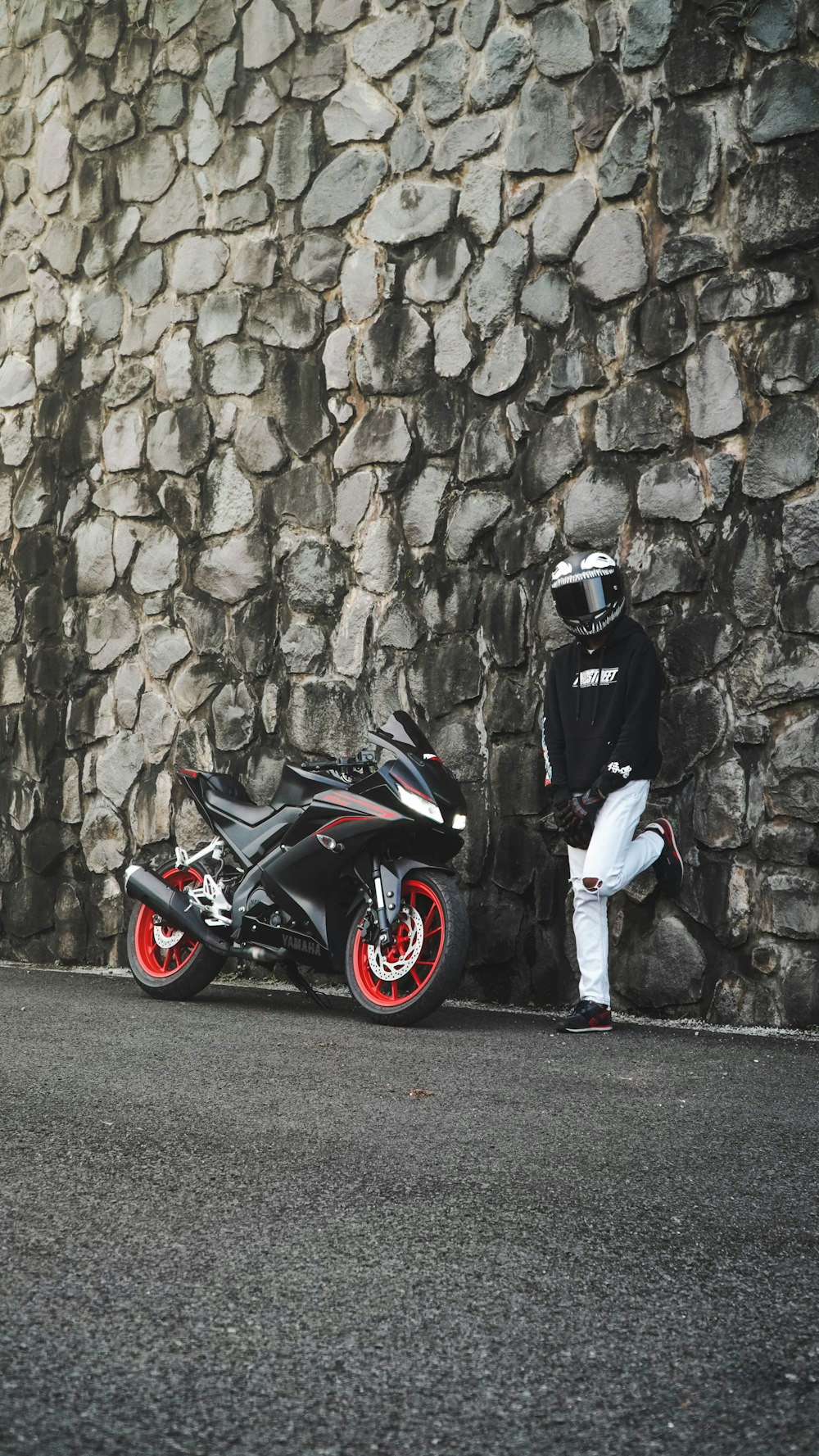 a man standing next to a motorcycle next to a stone wall