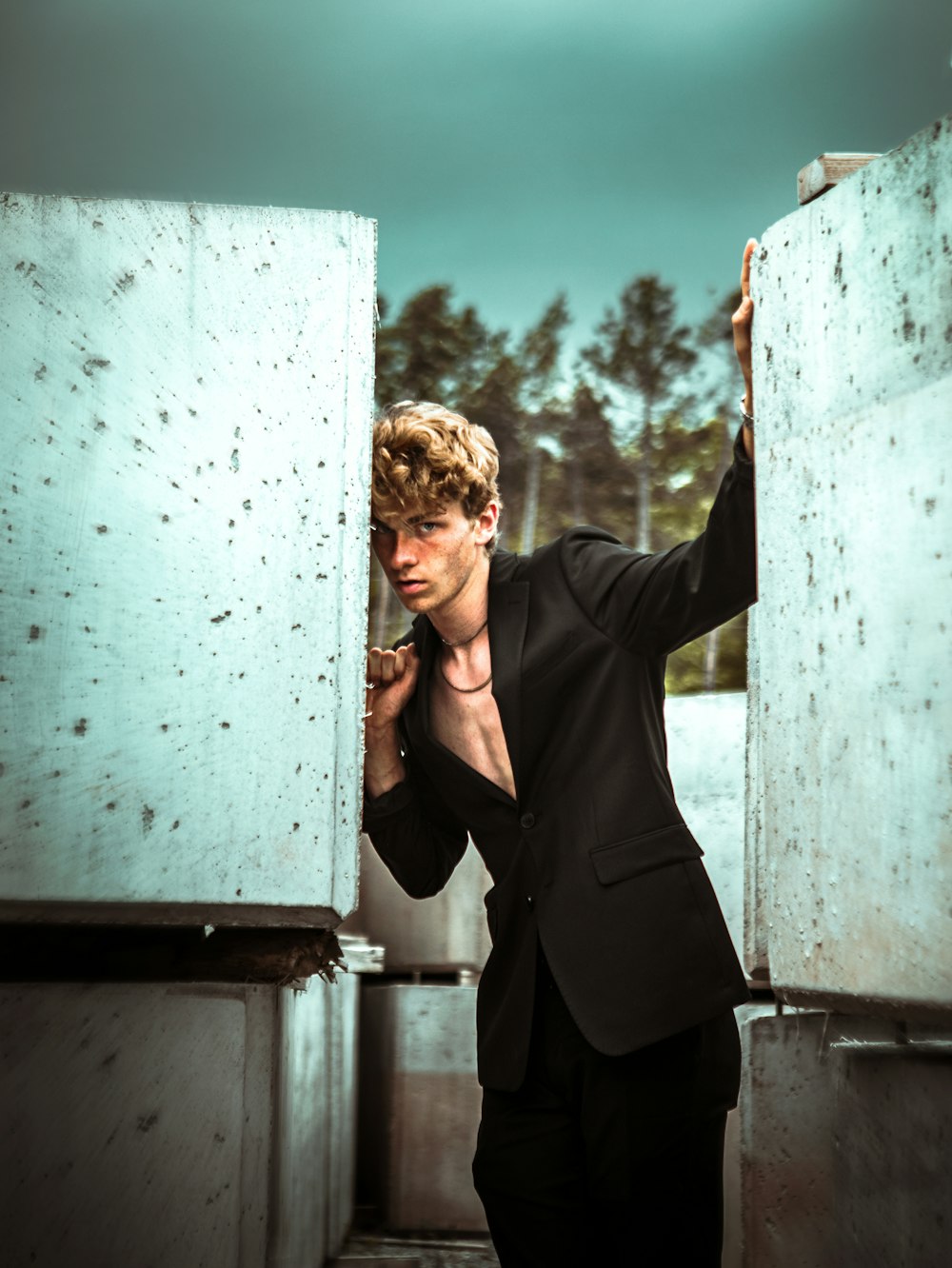 man in black blazer leaning on white wall