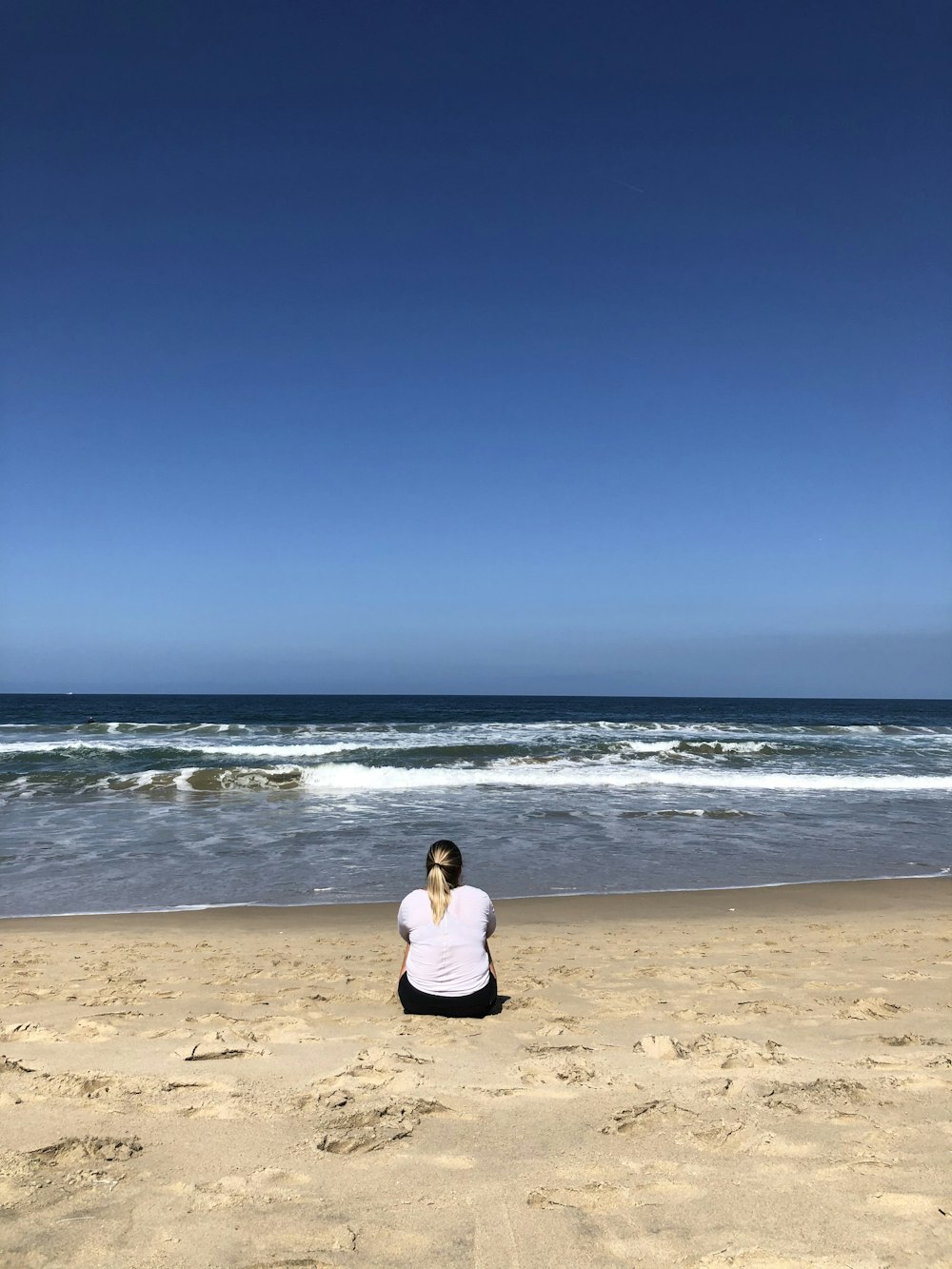 woman in white long sleeve shirt sitting on beach shore during daytime
