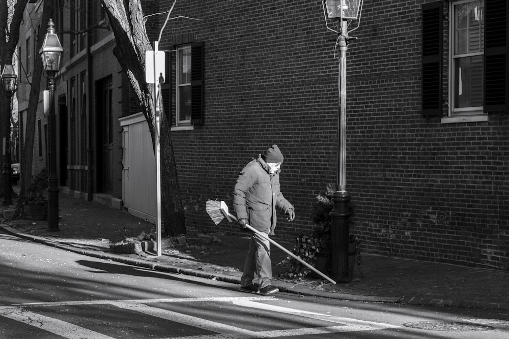man in white jacket and black pants holding a stick walking on the street
