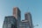 Several modern high-rise buildings under construction with cranes on top, set against a clear blue sky. The buildings have a grid-like pattern of windows and are predominantly made of concrete and glass.