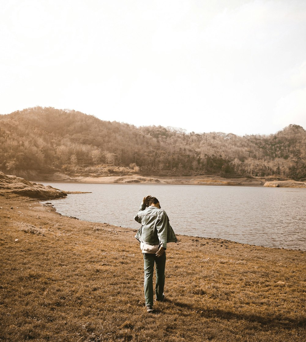 man in gray jacket standing on brown field near body of water during daytime