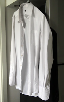 A crisp white button-down shirt neatly folded on a black wooden table.