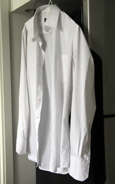 Crisp white blouse with structured collar and pearl buttons on a hanger.
