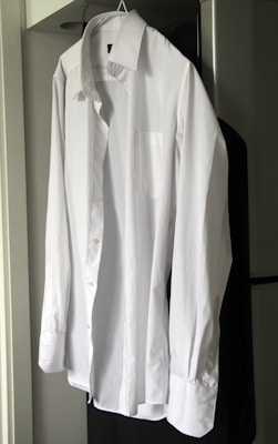 A casual white button-up shirt paired with tailored black trousers, displayed on a wooden hanger.