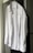A neatly ironed white dress shirt hangs on a hanger against a neutral background. The shirt is buttoned up with long sleeves, a collar, and a front pocket.