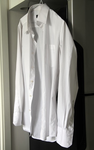 Close-up of a finely tailored white shirt on a wooden hanger against a neutral background.