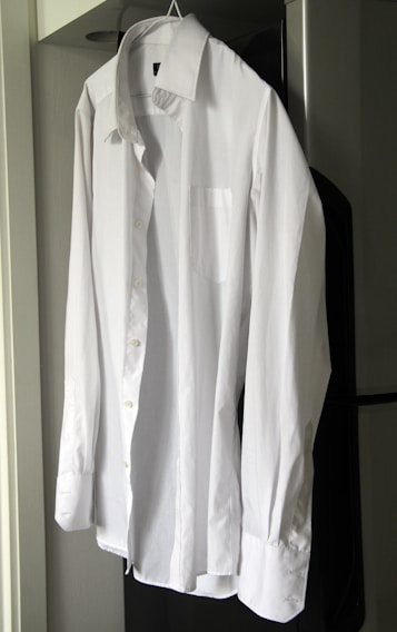 A close-up of a perfectly pressed white shirt hanging neatly on a hanger against a clean blue and white background.