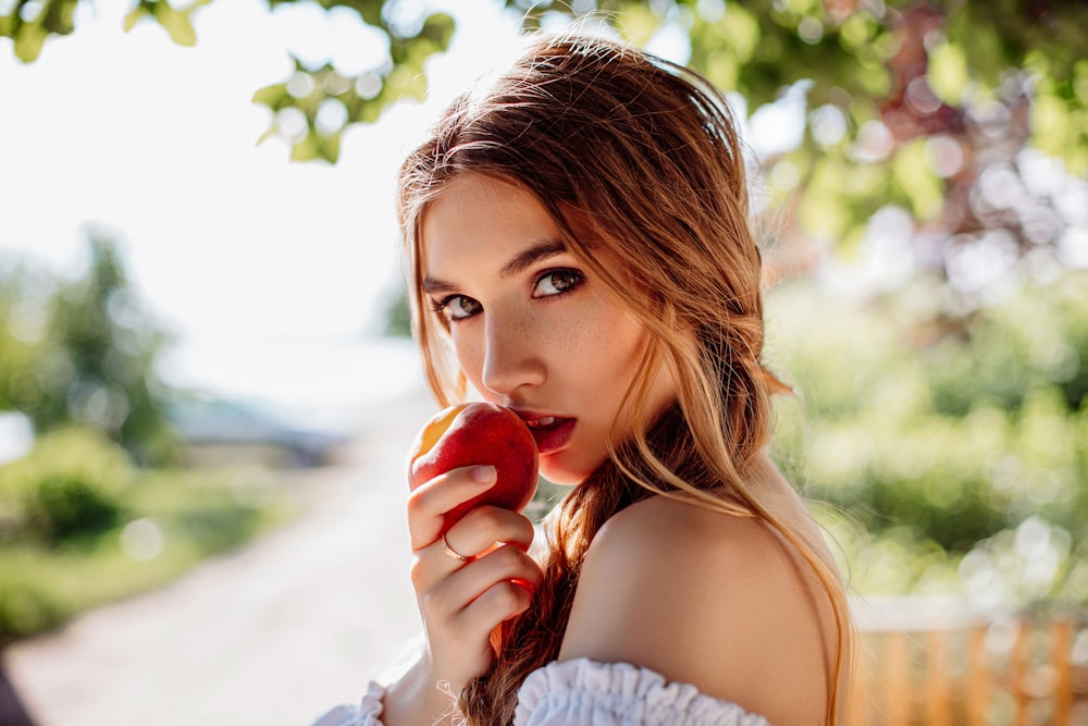 woman in white off shoulder shirt holding red apple