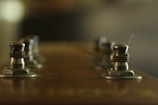 A close-up view of guitar tuning pegs on a headstock, with a focus on metallic knobs and coiled strings. The image is softly lit and slightly out of focus in the background.