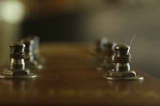A set of polished tuning pegs arranged on a wooden table with city skyline blurred behind.