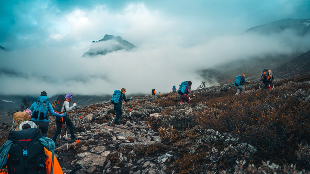 people hiking on rocky mountain under white clouds during daytime