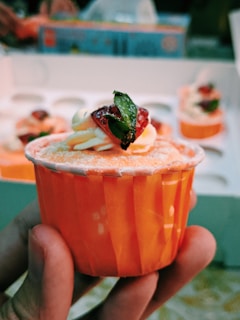 Close-up of a hand holding a pink nude frosted sugar-free cupcake with mint green packaging.