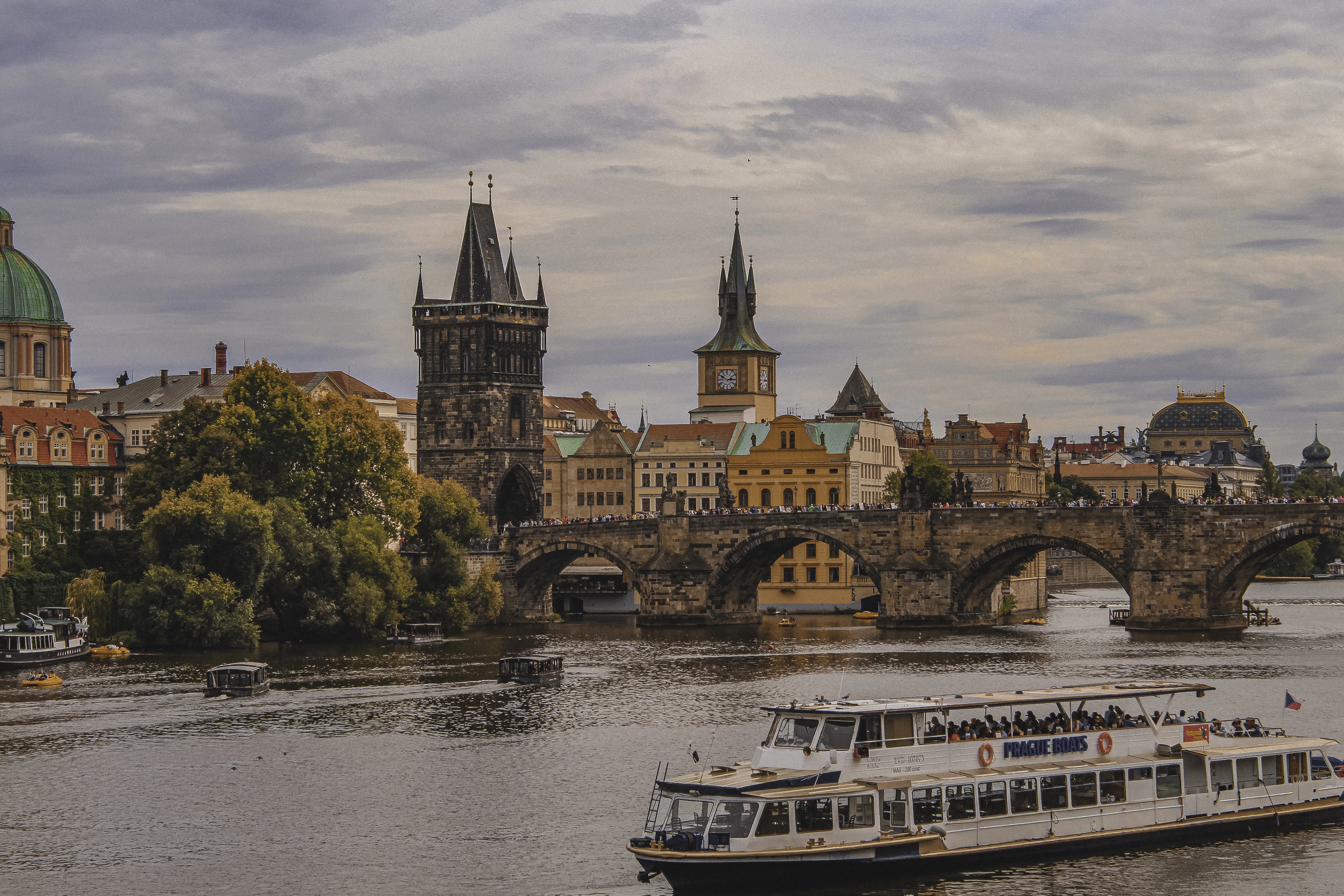 Charles Bridge and the Old Town Bridge Tower seen from across the Vltava, with a sightseeing boat passing in the foreground