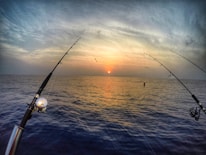 An experienced angler casting a lure rod into a calm sea during golden hour.