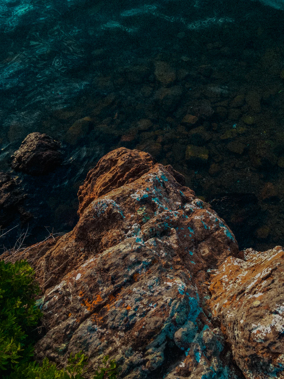 Rocky cliff overlooking calm water with sky visible through gaps between rocks and waves