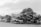 A large pile of crushed and stacked vehicles forms a chaotic mountain in what appears to be a junkyard or scrapyard. The cars are mostly stripped and stacked haphazardly on top of one another against a clear sky.