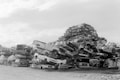 A large pile of crushed and stacked vehicles forms a chaotic mountain in what appears to be a junkyard or scrapyard. The cars are mostly stripped and stacked haphazardly on top of one another against a clear sky.