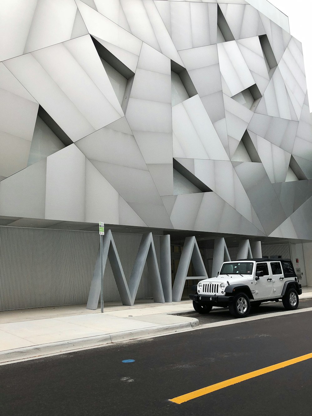 SUV blanco y negro estacionado junto a un edificio de concreto blanco durante el día