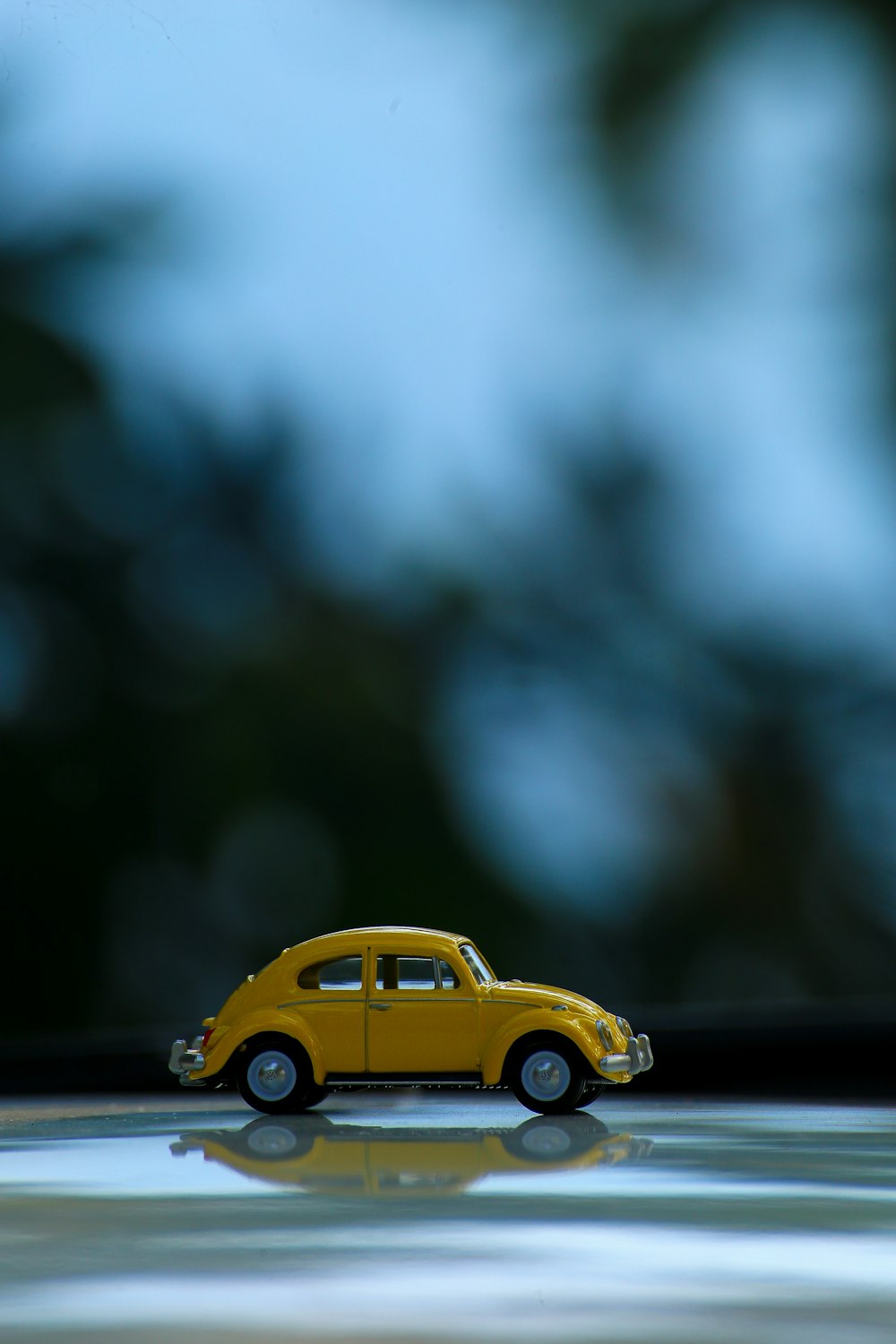 yellow volkswagen beetle on black asphalt road in tilt shift lens