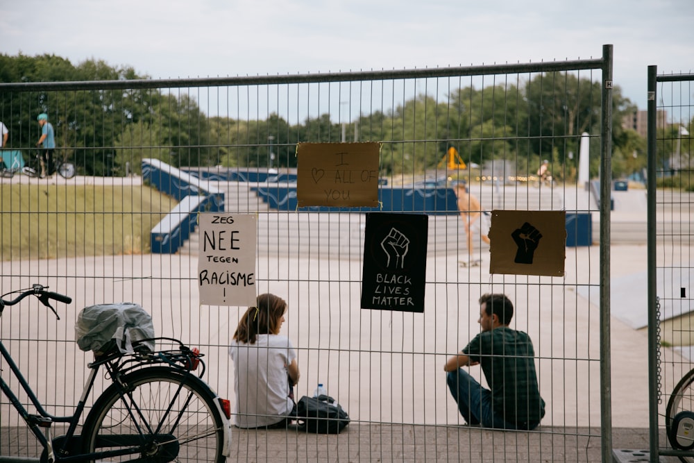 man and woman sitting on black metal fence during daytime