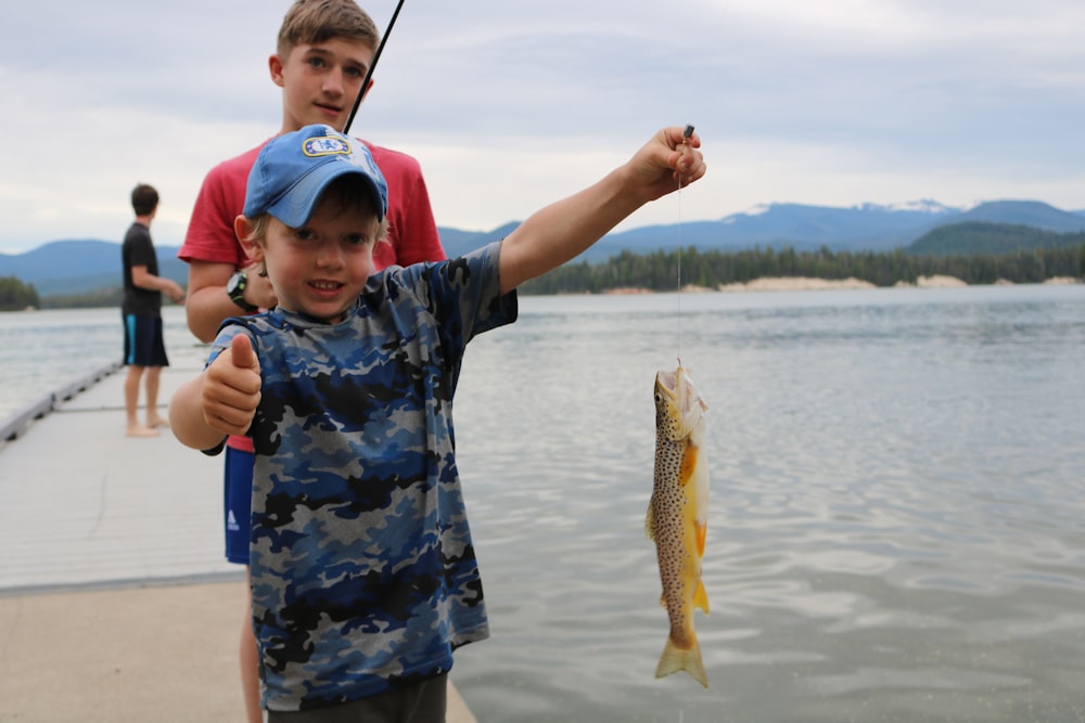 boy in blue and white camouflage shirt holding fish