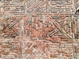 An arrangement of bricks forming a patterned design on a wall, featuring a mix of horizontal and diagonal placements creating geometric shapes. The bricks vary in shades of red and brown with some areas covered in mortar.