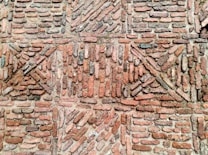 An arrangement of bricks forming a patterned design on a wall, featuring a mix of horizontal and diagonal placements creating geometric shapes. The bricks vary in shades of red and brown with some areas covered in mortar.