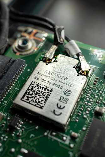 Close-up view of a computer circuit board featuring a Wi-Fi module with labels and a QR code. The module is connected to the board with visible soldered connections and surrounding electronic components.