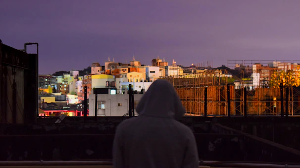 Evening city skyline with a person wearing a Lumina Apparel windbreaker, the fabric catching the soft glow of streetlights.