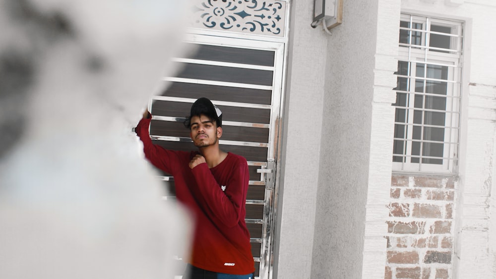 Hombre con camisa roja de manga larga de pie junto a la puerta de acero rojo y blanco durante el día