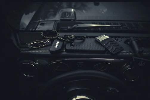 A compact dash cam beside a car key and sunglasses on a dashboard.