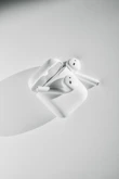 A pair of wireless earbuds resting beside a smartphone on a minimalist white surface.