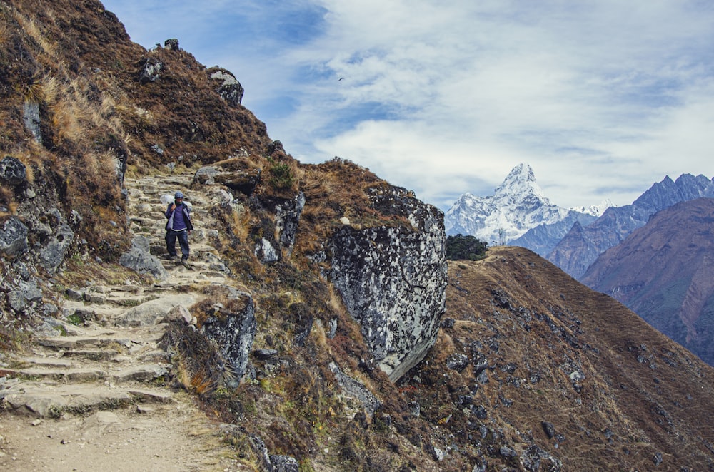Persona en chaqueta negra y pantalones negros de pie en la montaña rocosa durante el día