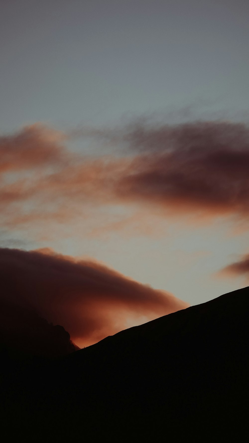 silhouette of mountain under cloudy sky during sunset