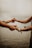 Two hands reaching out and holding each other, set against a serene background of a calm, blurred seascape. The image conveys a sense of connection and tenderness.