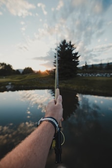 A beginner angler holding a freshly caught bluegill by a calm suburban lake at sunset.