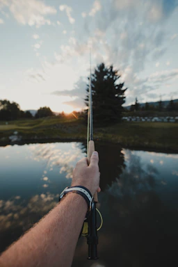A friendly fisherman holding a fishing rod by a calm river at sunset.