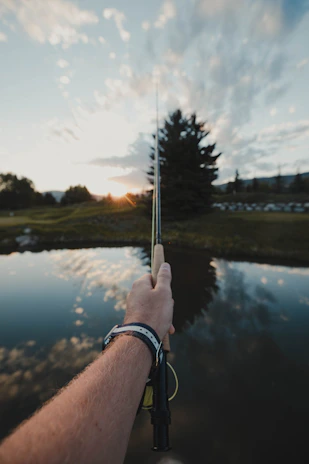 A man over 50 casting a fishing line into a serene forest lake at sunset.