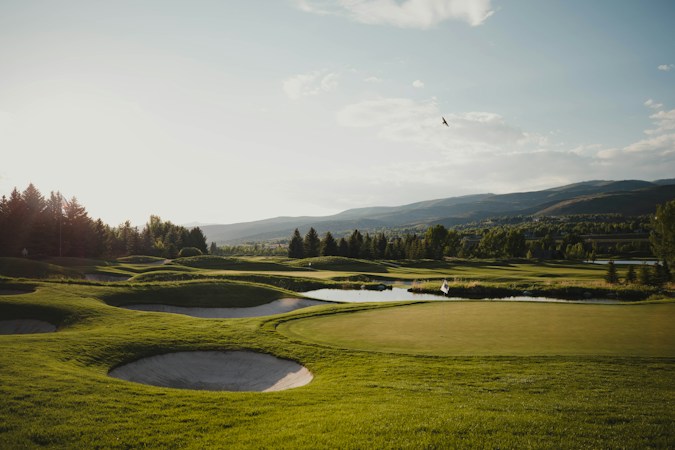 A wide green golf course fairway lined with trees, the kind of permanent open space that gives Seven Hills golf frontage lots their premium