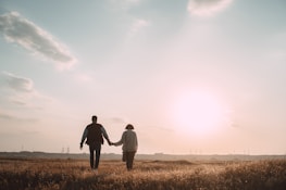 A serene outdoor setting with a couple walking hand in hand during sunset.