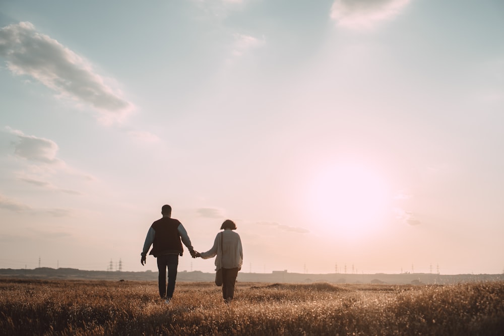 couple se tenant la main en marchant sur un champ d’herbe pendant la journée