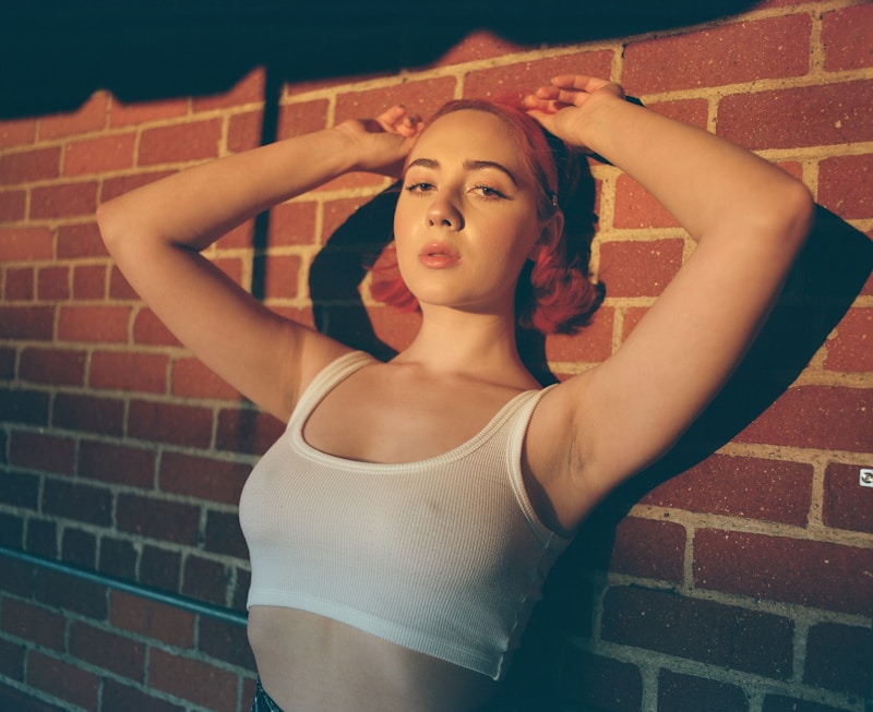 woman in white tank top standing beside brown brick wall