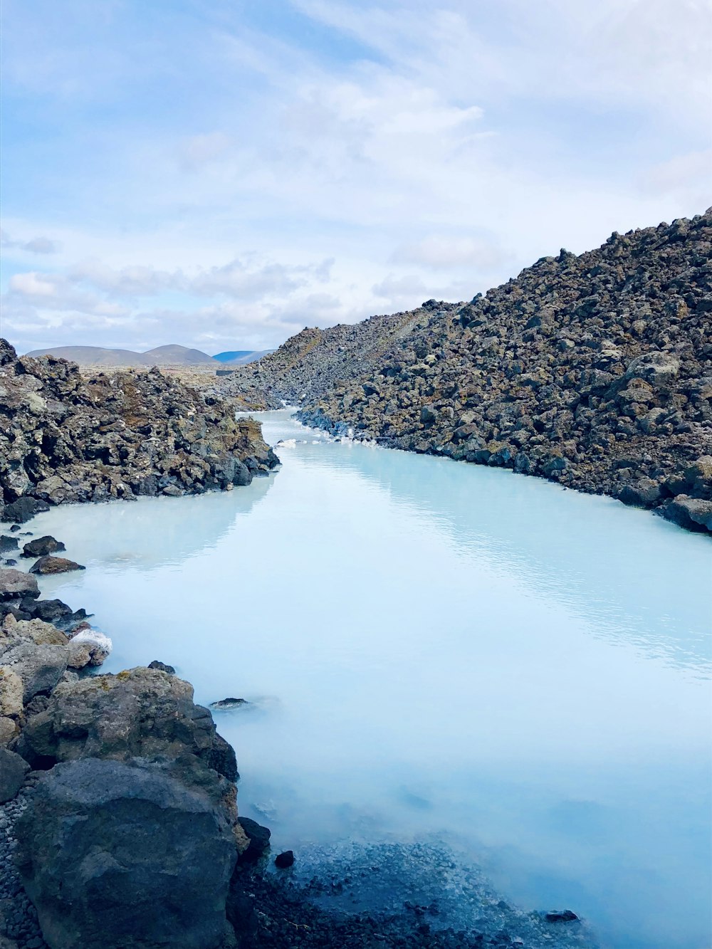 gray rocky mountain beside river under white clouds during daytime