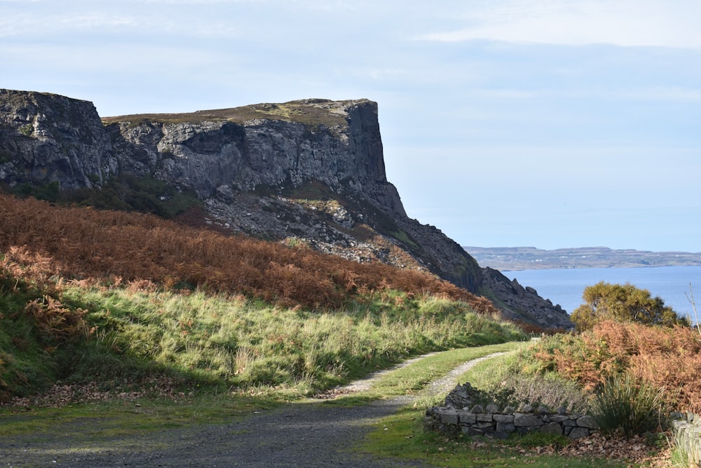 green grass field near brown rock formation under white clouds during daytime