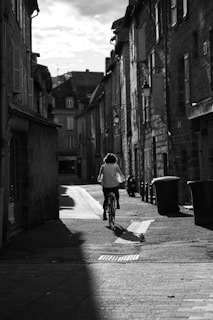 man in white shirt riding bicycle on street in grayscale photography