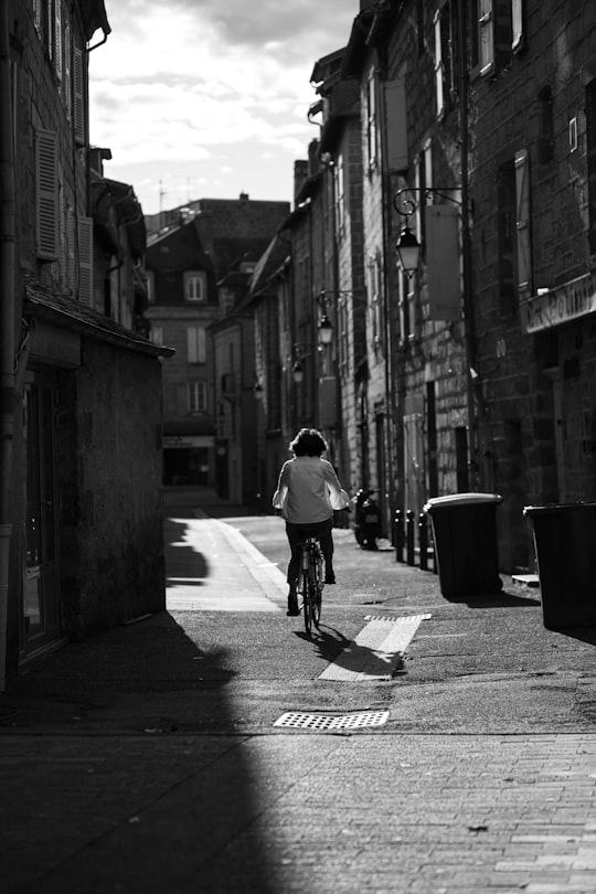 man in white shirt riding bicycle on street in grayscale photography in Brive-la-Gaillarde France
