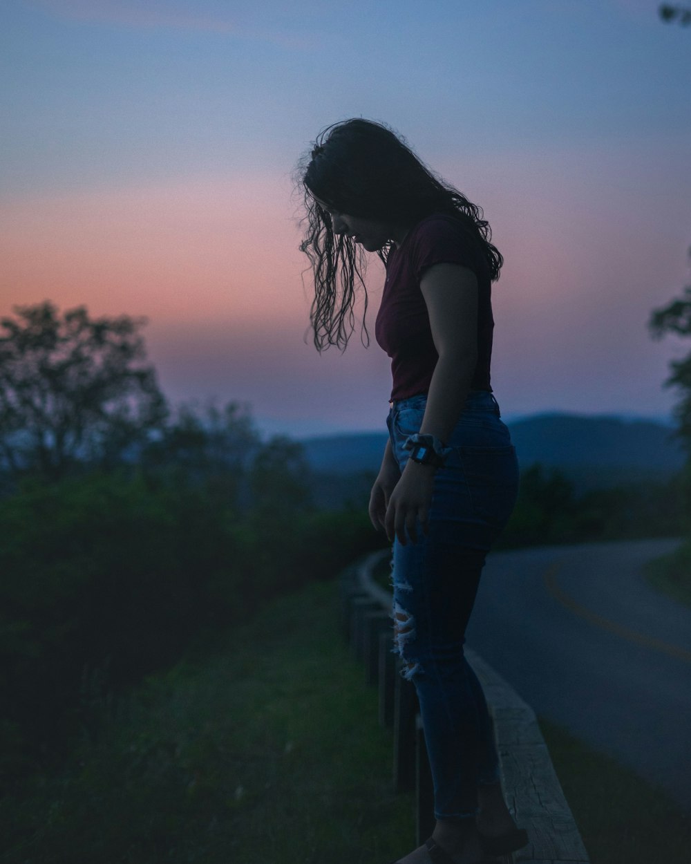 woman in black tank top and blue denim jeans standing on green grass field during sunset