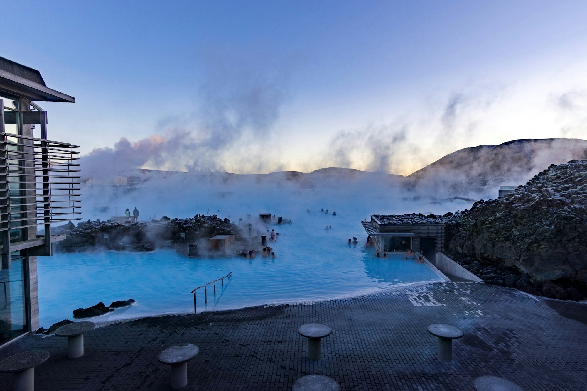 Iceland's famous Blue Lagoon with the natural steam raising to the sky, the bright blue water and the sun setting in the background. 