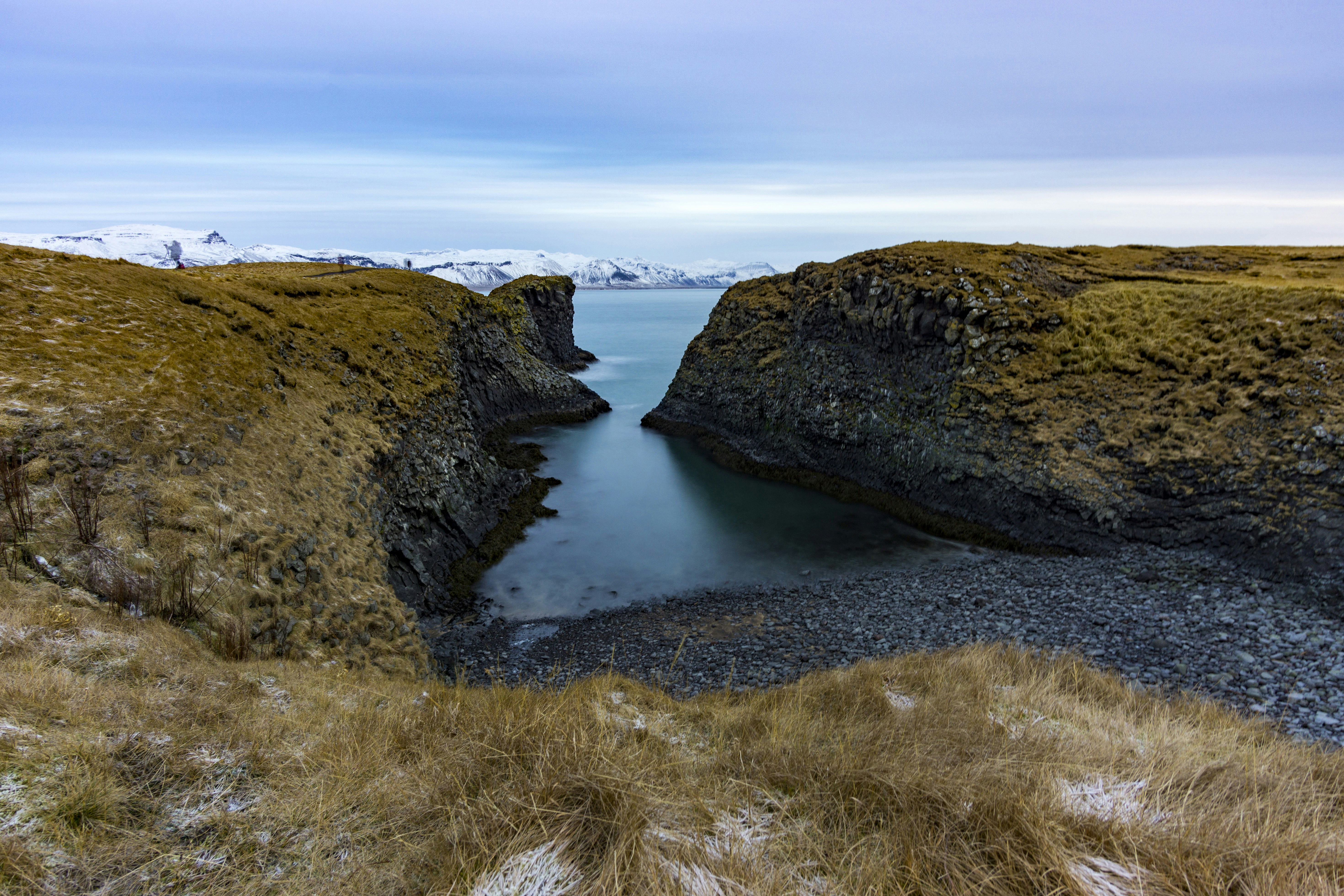 green and brown mountain beside body of water under blue sky during daytime